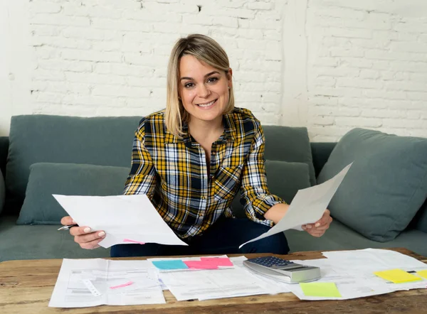 Happy attractive housewife or entrepreneur woman paying bills, calculating costs, charges, mortgage, taxes with documents and calculator in living room. In success home and business finances concept.