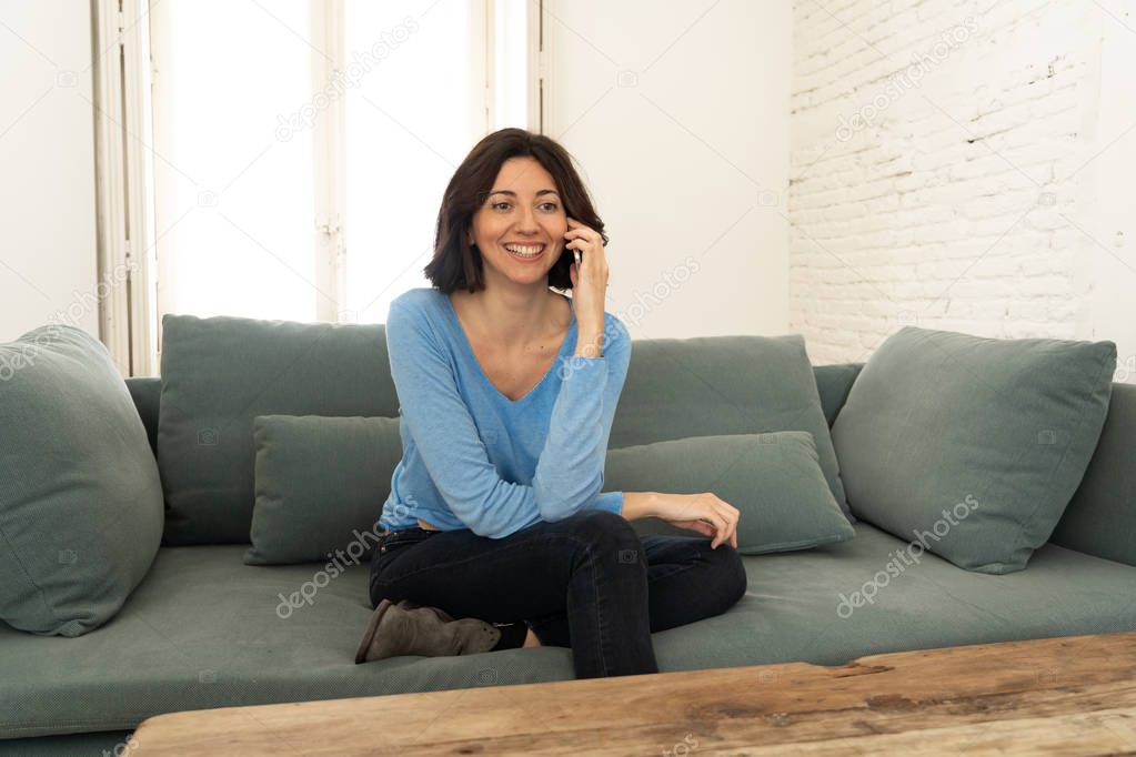 Lifestyle portrait of relaxed attractive woman talking on phone with friends smiling happy on the couch at home. In leisure internet, smartphone and social network concept.