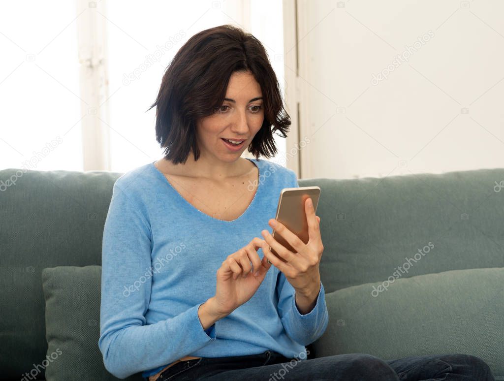 Lifestyle portrait of attractive woman on smart mobile phone Sending messages, chatting or in social media smiling happy on the couch at home. In leisure internet and social network addiction.