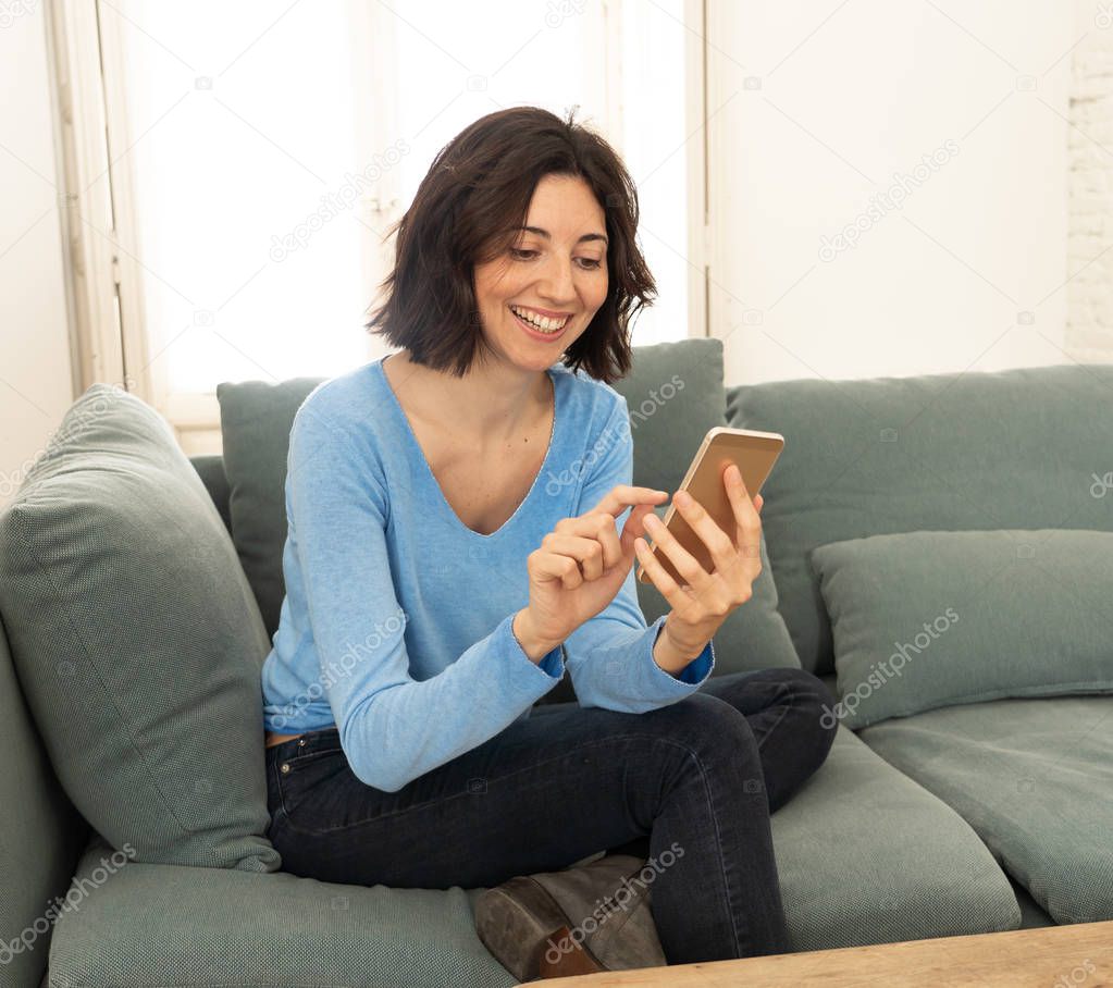 Lifestyle portrait of attractive woman on smart mobile phone Sending messages, chatting or in social media smiling happy on the couch at home. In leisure internet and social network addiction.