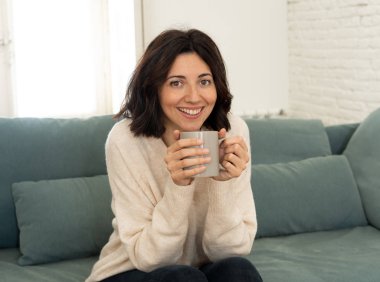 Sıcak kahve veya çikolata içen genç oldukça rahat kadın yaşam tarzı portre kanepede mutlu gülümseyerek evde mutlu ve rahat duygu. Boş zamanlarında, huzurlu yaşam, mutluluk yaşam tarzı kavramı.