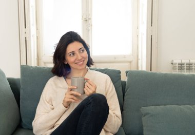 Sıcak kahve veya çikolata içen genç oldukça rahat kadın yaşam tarzı portre kanepede mutlu gülümseyerek evde mutlu ve rahat duygu. Boş zamanlarında, huzurlu yaşam, mutluluk yaşam tarzı kavramı.