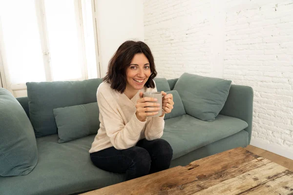 Lifestyle portrait of young pretty relaxed woman drinking hot coffee or chocolate feeling happy and cozy at home smiling happy on the couch. In leisure, peaceful life, happiness lifestyle concept.