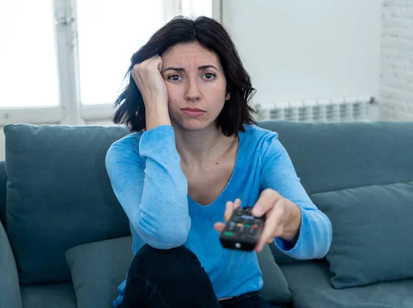 Young upset woman on sofa using control remote zapping bored of bad TV shows and programing . Looking disinterested, aloof and sleepless. People, too much bad television and Sedentary lifestyle.