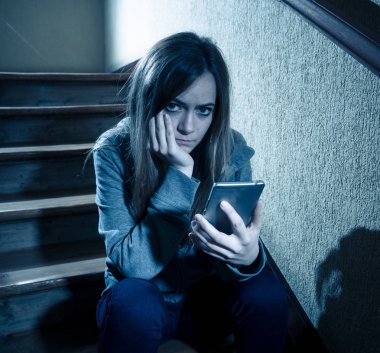 Yalnız, mutsuz, umutsuz ve istismar hissi merdiven üzerinde mobil akıllı telefon siting tarafından siber zorbalık üzücü depresif genç kız kızı kurbanı. Sosyal medya uygulamasında kısa mesaj ile bullied. koyu ışık