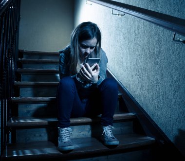 Yalnız, mutsuz, umutsuz ve istismar hissi merdiven üzerinde mobil akıllı telefon siting tarafından siber zorbalık üzücü depresif genç kız kızı kurbanı. Sosyal medya uygulamasında kısa mesaj ile bullied. koyu ışık