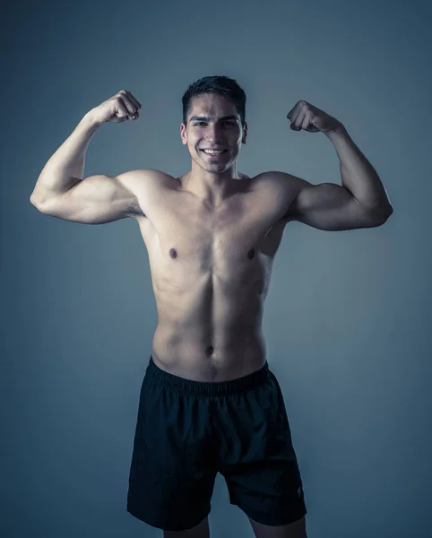 Portrait of strong handsome Athletic man isolated on neutral background. Mixed race latin fitness model posing showing biceps and strong body. In exercise, healthy lifestyle, workout and body care.