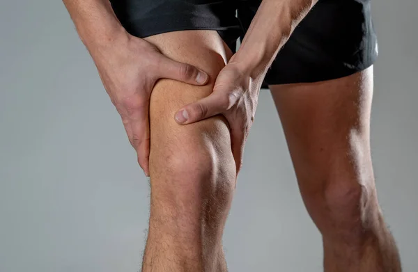 年轻的适合男子抱着膝盖与手在痛苦后遭受肌肉损伤断骨腿疼痛扭伤或抽筋在跑步锻炼 在身体疼痛和运动训练损伤和身体保健 — 图库照片