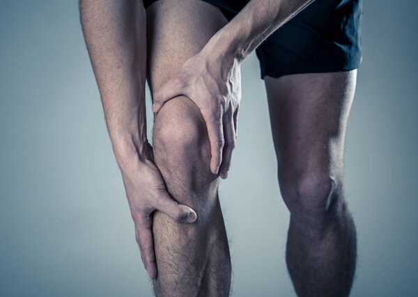 Young fit man holding knee with hands in pain after suffering muscle injury broken bone leg pain sprain or cramp during running workout. In Body pain and sport training injury and body health care.