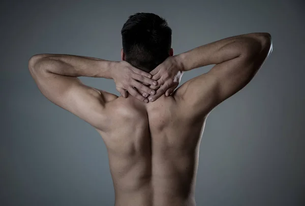 Young muscular fit man touching and grabbing neck and upper back suffering cervical pain after workout. Isolated on neutral background. In sport injury Incorrect posture problems and body health care.