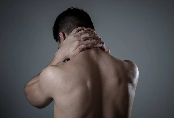 Young muscular fit man touching and grabbing neck and upper back suffering cervical pain after workout. Isolated on neutral background. In sport injury Incorrect posture problems and body health care.