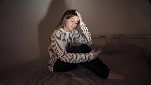 スマートフォン上の悲しい絶望的な若い十代の女の子は オンラインのいじめとハラスメントに苦しむ夜にベッドの上で座って孤独と絶望を伐採 ネットいじめとインターネット概念の危険性 — ストック写真