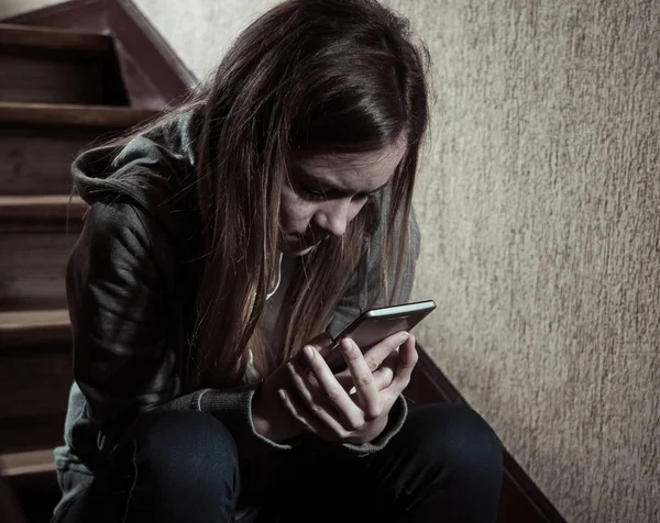 悲しい落ち込んだ若い十代の若者たちの少女は 階段上のモバイルスマートフォンの立地によるネットいじめの被害孤独 絶望的で虐待を感じています ソーシャルメディアアプリ上のテキストメッセージによっていじめ ダークライト — ストック写真