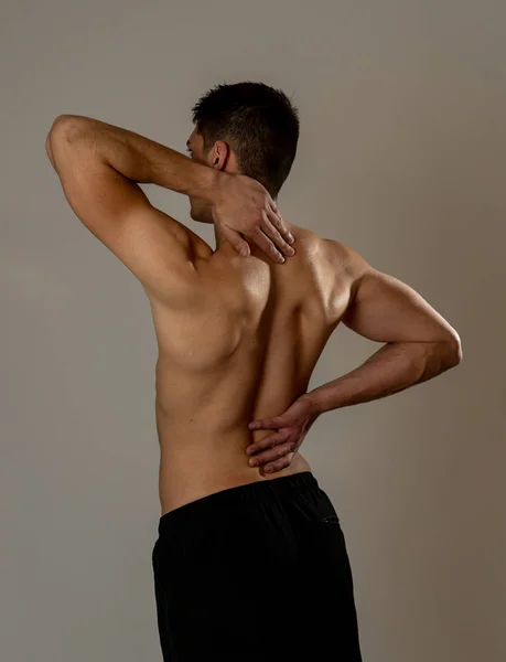 Young muscular fitness man touching and grabbing his neck and lower back suffering cervical pain isolated on neutral background. In sport and workout injury, Incorrect posture problems and body care. — Stock Image Young Muscular Fitness Man Touching Grabbing His Neck Lower Back Royalty Free Stock Images