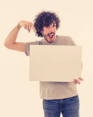 Komik ve iyi görünümlü milenyal adam gösteren ve metin için kopya alanı ile boş tahta işaret. Samimi ve heyecanlı genç şık adam reklam için boş poster tutuyor. Pazarlama konsepti.