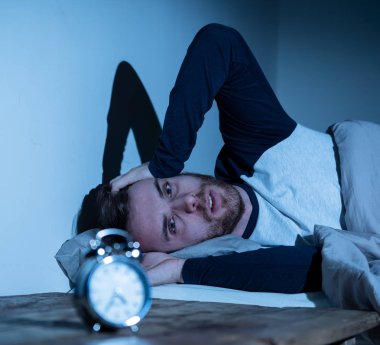 Uykusuz ve çaresiz genç beyaz adam Uykusuz geceleri uyku mümkün değil, hayal kırıklığına ve endişe saat uykusuzluk stres ve uyku bozukluğu kavramı muzdarip bakıyor.