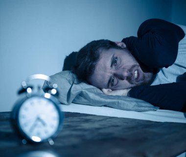 Uykusuz ve çaresiz genç beyaz adam Uykusuz geceleri uyku mümkün değil, hayal kırıklığına ve endişe saat uykusuzluk stres ve uyku bozukluğu kavramı muzdarip bakıyor.