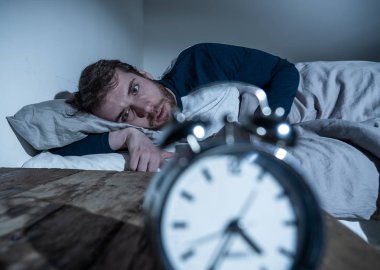 Ruh sağlığı, uykusuzluk ve uyku bozuklukları. Sinirli ve umutsuz uykusuz adam alarm saat uyanık gece uyanma anksiyete İşteki stres neden acı uyku mümkün değil bakıyor.