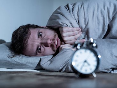 Ruh sağlığı, uykusuzluk ve uyku bozuklukları. Sinirli ve umutsuz uykusuz adam alarm saat uyanık gece uyanma anksiyete İşteki stres neden acı uyku mümkün değil bakıyor.