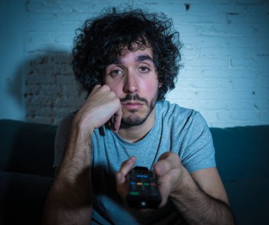 Başka bir film veya gece geç saatlerde göstermek için TV uzaktan kumanda zap kullanarak kanepede genç sıkılmış adam. İlgilenmiyor ve uykusuz görünüyorsun. Eğlence Insanlar uykusuzluk ve sedanter yaşam tarzı kavramı.