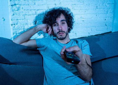 Başka bir film veya gece geç saatlerde göstermek için TV uzaktan kumanda zap kullanarak kanepede genç sıkılmış adam. İlgilenmiyor ve uykusuz görünüyorsun. Eğlence Insanlar uykusuzluk ve sedanter yaşam tarzı kavramı.