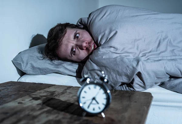 Mental health, Insomnia and sleeping disorders. Frustrated and hopeless sleepless man looking in distress at alarm clock awake at night not able to sleep suffering anxiety caused by stress at work.