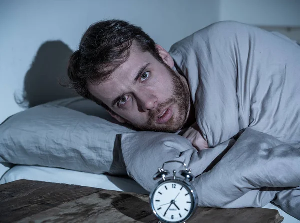 Mental health, Insomnia and sleeping disorders. Frustrated and hopeless sleepless man looking in distress at alarm clock awake at night not able to sleep suffering anxiety caused by stress at work.