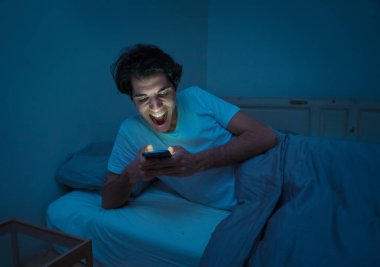 Addicted Man sohbet ve yatakta gece geç saatlere kadar akıllı telefon ile Internette sörf. Sıkılmış, uykusuz ve kasvetli ışık ile karanlık odada yorgun. Uykusuzluk ve mobil bağımlılık kavramı.