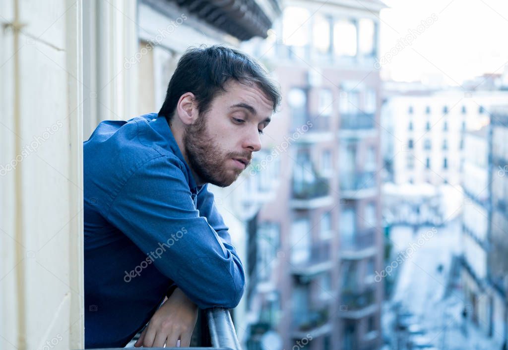Happy good looking bearded man smiling enjoying urban view on outdoor balcony. Happy young hipster in European city relaxing on room balcony. Home comfort lifestyle and traveling around Europe.