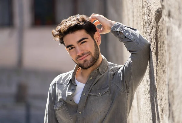 Attractive stylish latin young man posing sensual looking at the camera with fashion and stylish clothes in urban european city outdoors. In People beauty Youth fashion trends and travel around Europe.