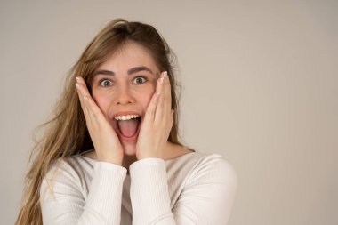 Güzel genç sarışın genç kadın mutlu yüz sürpriz jestleri görünümlü ve şok edici ve iyi bir şey işaret yapıyor. İnsan yüz ifadeleri ve duygular. Kopya alanı ile portre.