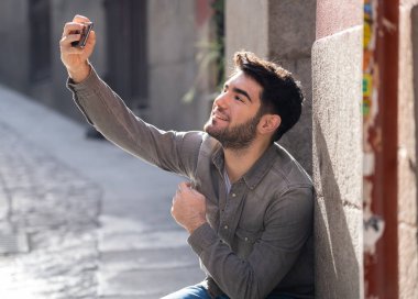 Heyecanlı Trendy genç adam selfie veya Avrupa şehir Caddesi veya üniversite kampüsünde tatil akıllı cep telefonu bloglama alarak. Tatil ve teknoloji bağlantı ve sosyal medya konsepti.