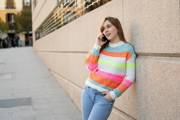 Pretty happy teenager woman talking on mobile smart phone outside city street. Beautiful stylish college student wearing fashion clothes feeling relaxed and free. Lifestyle, beauty and technology use.