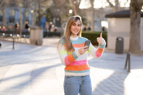 Pretty happy student woman chatting online on smart phone using social media apps outside city street. Beautiful teenager wearing stylish clothes feeling free. People, lifestyle and technology use.