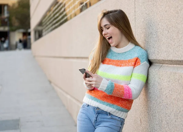 Pretty happy student woman chatting online on smart phone using social media apps outside city street. Beautiful teenager wearing stylish clothes feeling free. People, lifestyle and technology use.