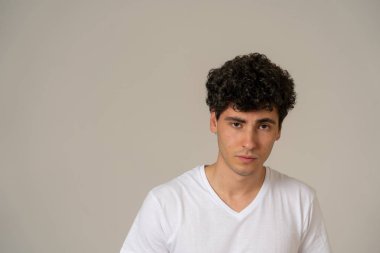 Onun 20s genç çekici şık moda adam rahat giysiler ve nötr arka plan karşı poz koyu kıvırcık saç seksi görünümlü. Tatlı ve erkeksi modelportresi. İnsanlar ve Güzellik kavramı.