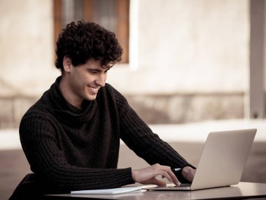 Yakışıklı genç adam bir Avrupa şehir kahve dükkanında teras dışında dizüstü bilgisayar üzerinde çalışıyor. Öğrenci Duygu mutlu ve memnun. Avrupa'da online eğitim ve teknoloji konsepti nde seyahat.