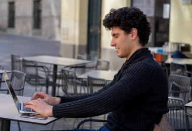 Yakışıklı genç adam bir Avrupa şehir kahve dükkanında teras dışında dizüstü bilgisayar üzerinde çalışıyor. Öğrenci Duygu mutlu ve memnun. Avrupa'da online eğitim ve teknoloji konsepti nde seyahat.