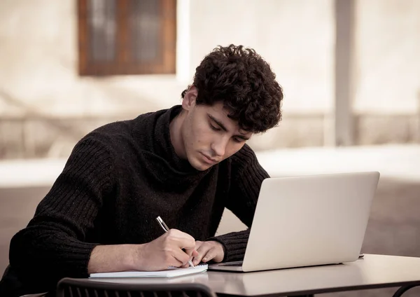 Handsome young man working on laptop computer outside terrace in an european city coffee shop. Student Feeling happy and satisfied. In travel around europe online education and technology concept.
