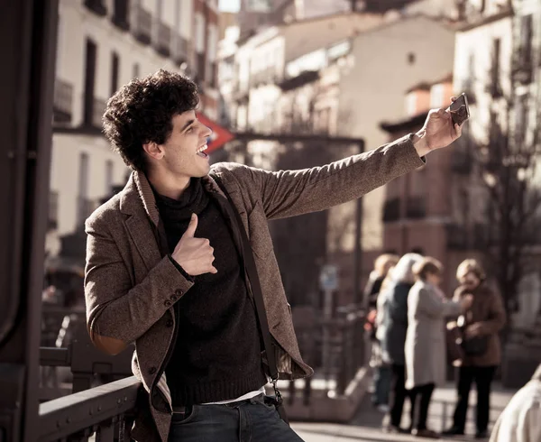 Heyecanlı Trendy genç adam selfie veya Avrupa şehir Caddesi veya üniversite kampüsünde tatil akıllı cep telefonu bloglama alarak. Tatil ve teknoloji bağlantı ve sosyal medya konsepti.