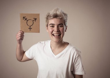 İyi görünümlü mutlu ve gururlu trans genç bir karton plaka üzerine çizilmiş transseksüel sembolü tutan. Cinsiyet kimliği ve çeşitliliğinin kavramsal imgesi. İnsan hakları ve eşitlik kampanyası.