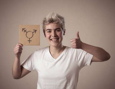 İyi görünümlü mutlu ve gururlu trans genç bir karton plaka üzerine çizilmiş transseksüel sembolü tutan. Cinsiyet kimliği ve çeşitliliğinin kavramsal imgesi. İnsan hakları ve eşitlik kampanyası.