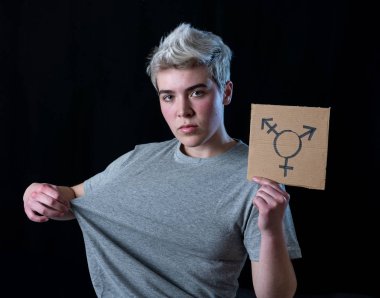 İyi görünümlü mutlu ve gururlu trans genç bir karton plaka üzerine çizilmiş transseksüel sembolü tutan. Cinsiyet kimliği ve çeşitliliğinin kavramsal imgesi. İnsan hakları ve eşitlik kampanyası.