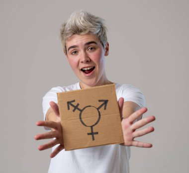 Good looking happy and proud trans teenager holding the symbol of the transgender drawn on a cardboard plate. Conceptual image of gender identity and diversity. Human rights and equality campaign. clipart