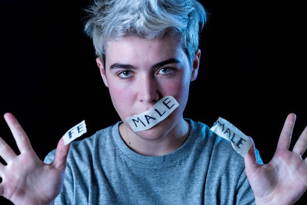 Handsome transgender teen with mouth sealed with male and female word written in Tape. Conceptual image of breaking silence about own gender identity, transgender pride and freedom concept.