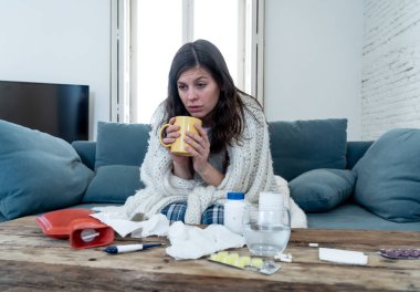Hasta genç kadın kanepede oturan sıcak içecek soğuk algınlığı ilacı içerken baş ağrısı burun ağrısı ve yüksek sıcaklık ile rahatsız hissediyorum işe gitmek mümkün değil. Sağlık ve tıbbi kavram.