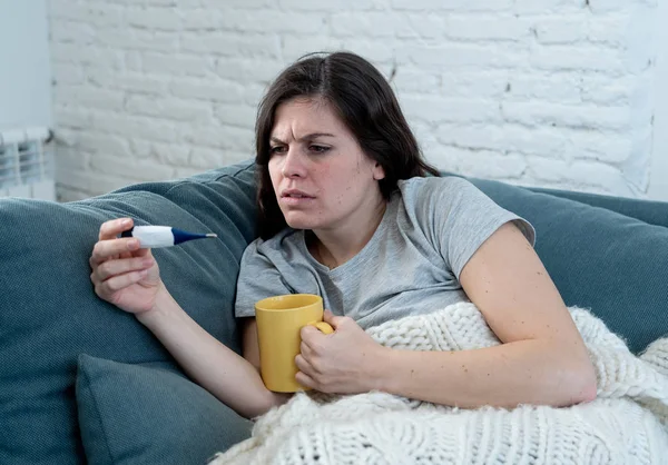 保健和医疗 生病的妇女躺在沙发上在家里不适头痛头痛鼻子检查高温与温度计感觉疲劳和不安不能去上班 — 图库照片