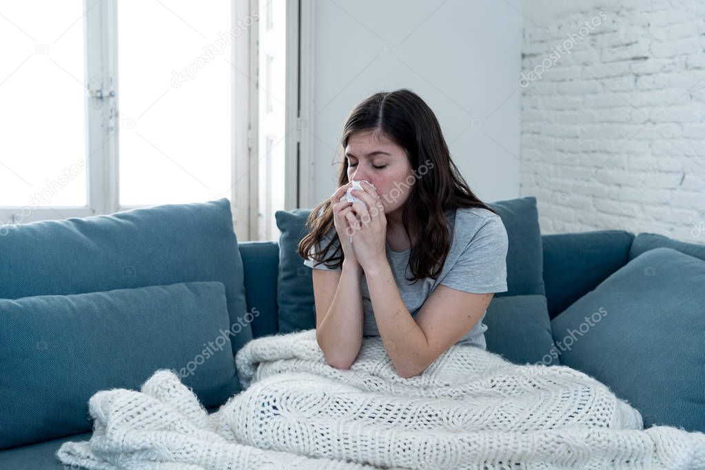 Sick woman on sofa sneezing and blowing her nose with allergy, hay fever or cold feeling unwell, fatigue and restless not being able to go to work. Lifestyle portrait In Health Care and medical.