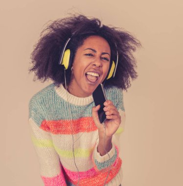 Muhteşem ve mutlu Afrikalı Amerikalı kadın kulaklık şarkı ve nötr arka plan üzerinde dans akıllı telefon müzik uygulaması dinlerken renkli portre. İnsanlarda Müzik Teknolojisi ve Mutluluk.