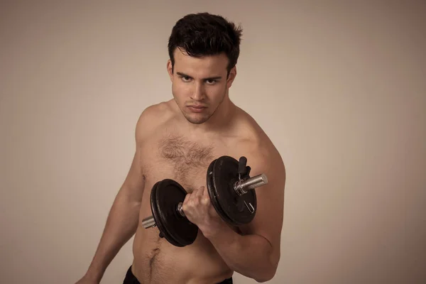 Portrait of young muscular built athlete man working out doing exercises and posing with dumbbells, bodybuilder male naked torso lifting weights in Fitness sports Body care and healthy lifestyle.